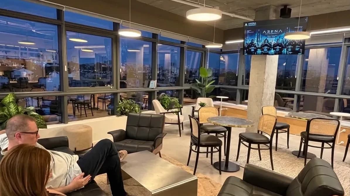 The firm's lounge at dusk, the city through the glass and a lit screen above the floor.
